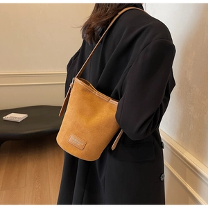 Detail of a ginger yellow PU leather bucket bag featuring a stitched brand logo and strap