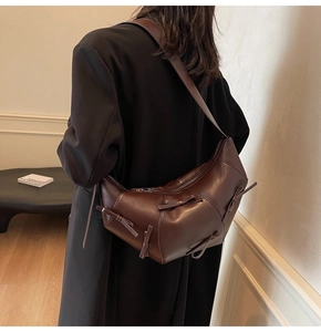 Détail d'un sac à bandoulière marron foncé avec nœuds papillon dans un décor intérieur