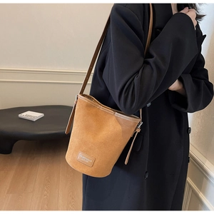 Detail of tan faux leather bucket bag with brand label on a long black coat