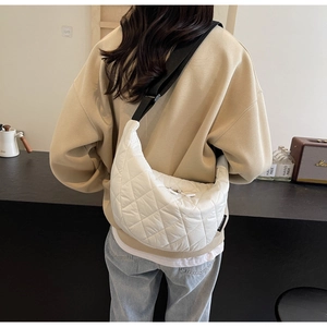 Detail of white quilted half-moon crossbody bag with black strap worn by a model