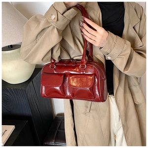 Close-up of a burgundy patent leather shoulder bag with decorative double front pockets