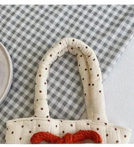 Close-up of quilted beige polka dot tote bag featuring a knitted orange bow detail