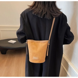 Detail of camel faux suede bucket bag with leather brand tag on black blazer