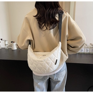 Detailed view of white quilted crescent bag with adjustable wide black strap on model