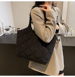 Close-up of black quilted nylon tote bag worn on shoulder in a stylish cafe setting