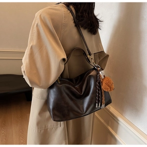 Detail of dark brown hobo shoulder bag with plush bear charm and tassel on a khaki coat