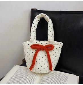 Detail of quilted white tote bag with black polka dots and orange knit bow on a chair