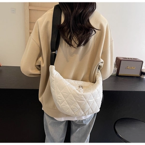 Detail of white quilted crescent bag with adjustable strap worn by model in a cozy setting