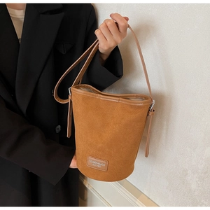Detailed view of a brown suede bucket bag featuring a slim strap and branded logo patch