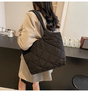 Detail of a large black quilted tote bag shown in a cozy cafe setting during autumn