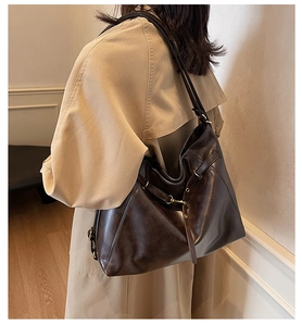 Detail of a large dark brown hobo tote bag in oily leather texture with buckle accent
