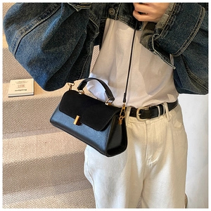 Detail of black crossbody bag with matte flap and gold metal clasp worn with denim jacket