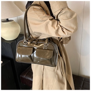 Detail view of olive green patent leather shoulder bag with dual front pockets on model