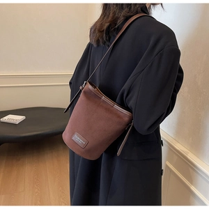 Detail showing brown matte leather bucket bag with slim shoulder strap and logo label