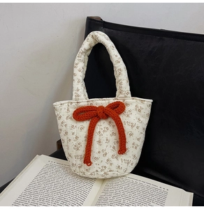 Detailed close-up of quilted floral shoulder bag with a large orange knit bow on a book