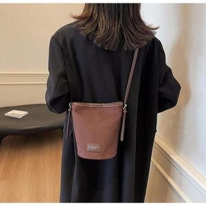 Brown faux suede bucket bag with leather strap and logo patch worn over a black blazer