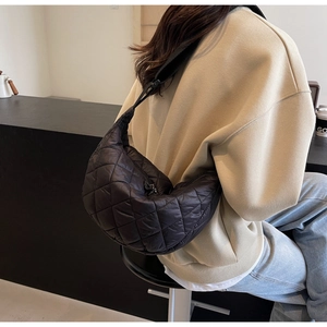 Detailed back view of a black quilted crescent crossbody bag worn over a beige sweater