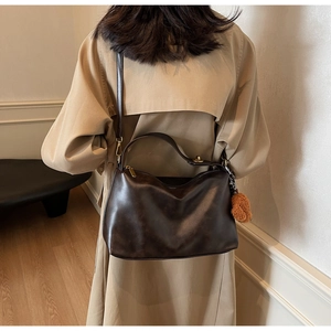 Detailed back view of a model wearing a deep brown leather handbag with a plush bear charm