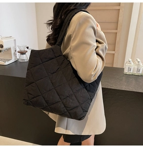 Detail of black quilted shoulder tote bag in nylon with wide strap shown on a model