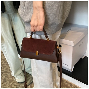 Detail of dark brown shoulder bag featuring suede and leather texture with golden hardware