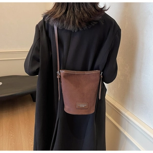 Detail view of brown suede bucket bag with leather brand tag showing shoulder strap texture