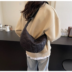 Detailed view of the black quilted nylon crescent bag worn on a model's back in a cafe
