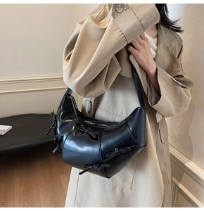 Détail du sac demi-lune noir avec nœuds porté sur un trench-coat beige élégant