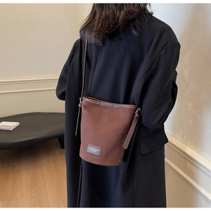 Detail view of a minimalist brown suede bucket bag worn with a black suit for autumn