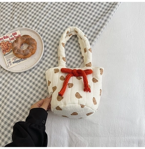 Close-up of white quilted fabric bucket bag featuring brown bear prints and orange bow detail