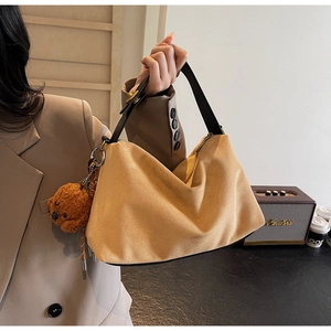 Close-up of soft khaki suede crescent bag with wide black strap and cute teddy charm