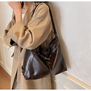 Detail of a large dark brown PU tote bag with gold hardware worn over a khaki trench coat