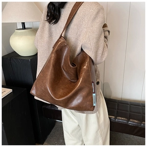 Detailed view of brown PU leather shoulder tote bag with woven brand labels and texture