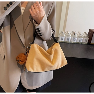 Detail of yellow suede handbag with black handles and brown plush bear charm pendant