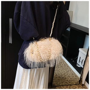 Detail of plush crossbody bag with pearl chain and heart charm worn by a model