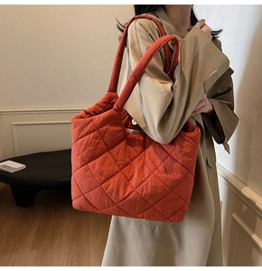 Detail of caramel orange quilted tote bag shown on model in a minimalist interior setting