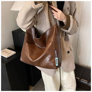 Detail of soft brown oiled PU leather texture and woven brand label on shoulder bag