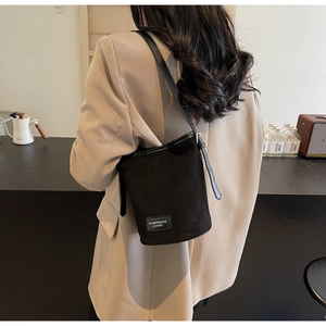 Detail view of black suede bucket bag with leather strap on a model wearing a khaki blazer