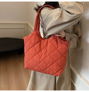 Close-up of bright orange quilted tote bag on shoulder with beige trench coat
