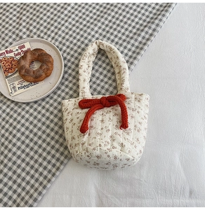 Detail of quilted floral handbag with red rope bow on soft cotton fabric background