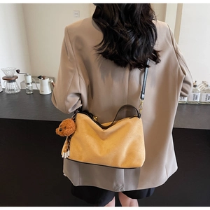 Detail of a ginger yellow PU shoulder bag with cute bear charm worn with beige suit