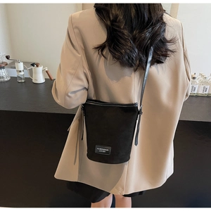 Detail of minimalist black PU leather bucket bag featuring a woven adjustable shoulder strap