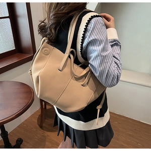 Lifestyle shot of a beige oversized faux leather tote bag worn by a model in a retro room