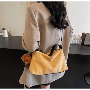 Chic mustard yellow suede crossbody bag with wide black strap and cute teddy bear charm