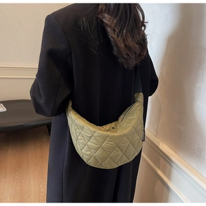 Detailed view of olive green quilted crescent crossbody bag worn with a black coat