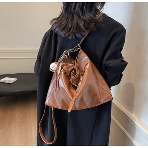 Detail view of brown leather large capacity hobo bag with baseball charm on shoulder