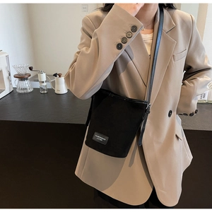 Close-up of black matte PU leather bucket bag with brand label on a beige blazer background