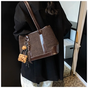 Close-up of brown textured fabric tote bag featuring leopard pompom and leather tassel charm