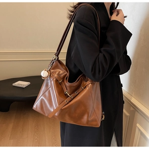 Detail of caramel brown PU leather tote bag with baseball charm on shoulder strap