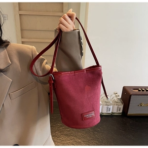 Detail of burgundy suede bucket bag featuring leather logo patch and handle texture