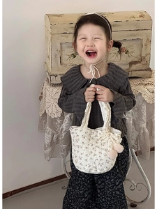 Détail d'un sac en toile fleurie crème avec dentelle et pompons roses sur un pull gris